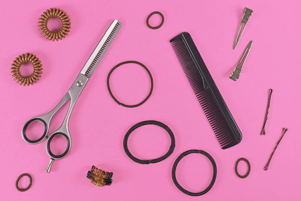Hair styling concept with elastic hair ties, hair pins, comb and thinning shears on pink background - Foto, Imagem