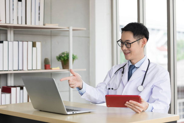 Ασιάτης γιατρός που μιλάει με ασθενή ή συνάδελφο μέσω online video chat με υπολογιστή στο νοσοκομείο - Φωτογραφία, εικόνα