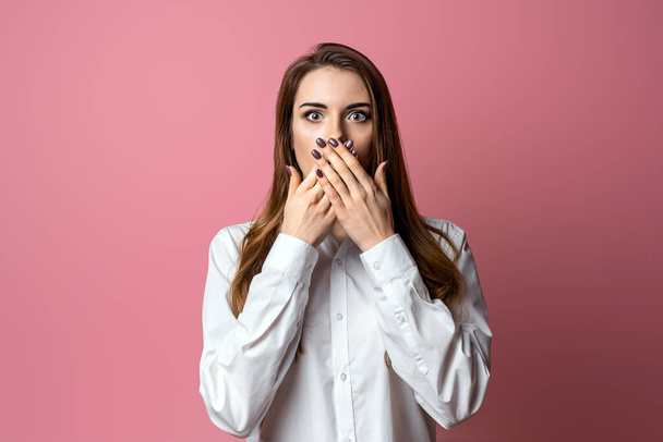 Portrait of scared brunette girl hold hands near mouth trembling fear, very terrified over scary creepy sound, standing in stupor over pink background - 写真・画像
