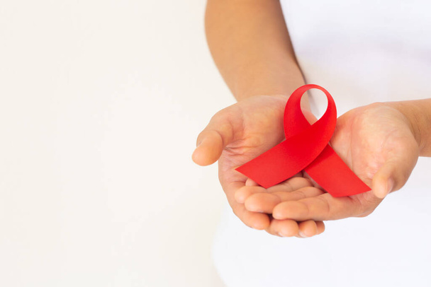 白い背景のコピースペースに赤いリボンを手に、 HIV/AIDSに生きる人々の連帯を象徴し、薬物乱用や飲酒運転の意識と予防のためのシンボル。健康コンセプト. - 写真・画像