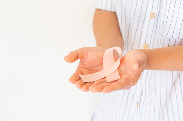 Ręczne trzymanie wstążki brzoskwiniowej na białym tle z przestrzenią do kopiowania, symbolem świadomości raka macicy i endometrium, Światowym Dniem Raka. Koncepcja opieki zdrowotnej lub szpitala i ubezpieczenia. - Zdjęcie, obraz