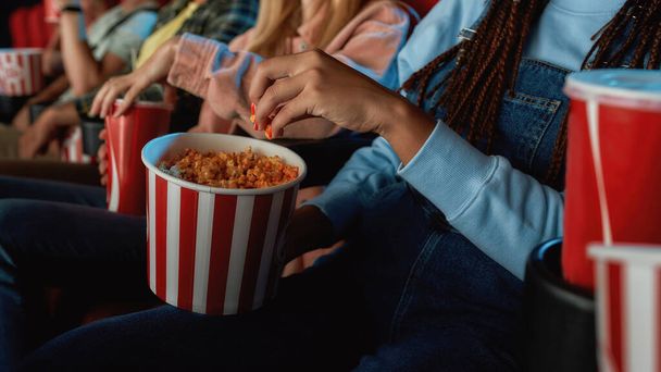 Close up of girl taking popcorn out of red with white basket while watching movie at the cinema - Fotoğraf, Görsel