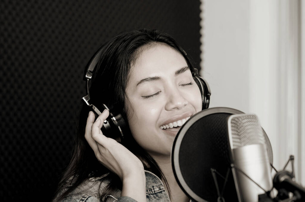 Aasialainen naislaulaja laulaa levytysstudiossa. Naislaulaja laulaa ja soittaa kitaraa. - Valokuva, kuva