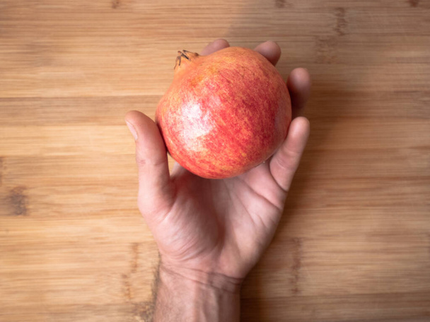 A top view of a person holding a pomegranate on a wooden table - Foto, imagen