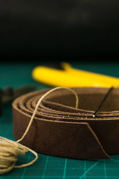 A vertical shot of a waxed sewing thread and a genuine leather roll on a craftsman's work table - Fotografie, Obrázek