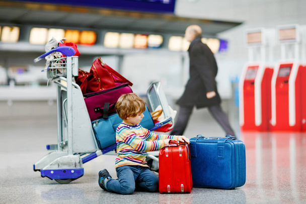 Χαρούμενο αγοράκι με μεγάλη βαλίτσα στο τερματικό στο διεθνές αεροδρόμιο. Νηπιαγωγημένο παιδί περιμένει την πτήση και πηγαίνει διακοπές. Οικογενειακός τρόπος ζωής. - Φωτογραφία, εικόνα