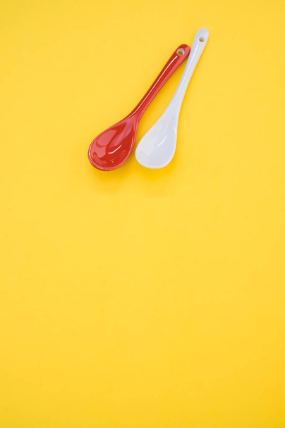 A vertical shot of small red and white spoons on a yellow background - Zdjęcie, obraz