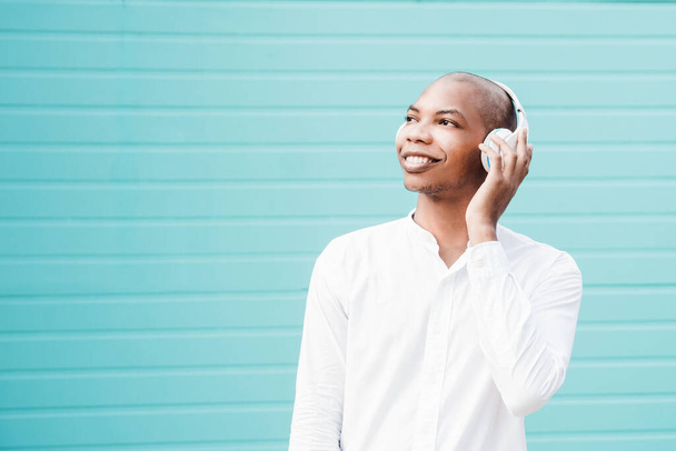 A cheerful Afro American with a white shirt and earphones posing at camera on a blue  background - Foto, immagini