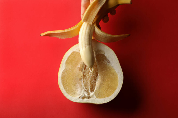 Mão feminina segura banana com leite condensado na fruta pomelo no fundo vermelho - Foto, Imagem