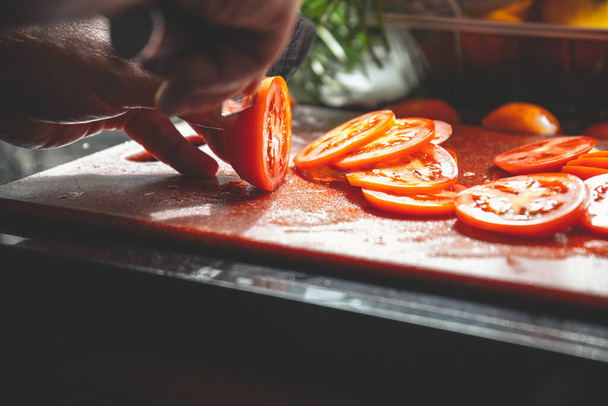 A beautiful shot of an unrecognizable chef cutting fresh tomatoes on a board for a massive party - Fotografie, Obrázek