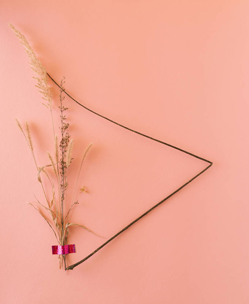 Morbida cornice delicata fatta di piante secche naturali e bastone di legno su sfondo rosa pastello. Estetica senza tempo. - Foto, immagini
