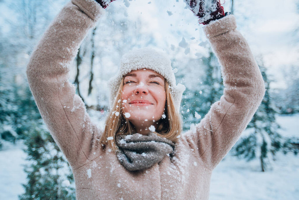 молодая счастливая девушка смеется и выливает на себя снег. снег на переднем плане - Фото, изображение