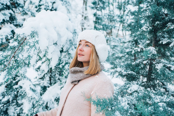Ένα νεαρό κορίτσι περπατά ανάμεσα στα χιονισμένα δέντρα το χειμώνα. - Φωτογραφία, εικόνα