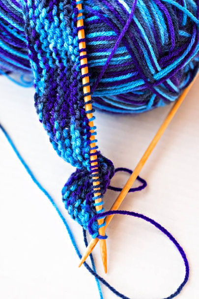 Knitting on wooden knitting needles from violet blue purple yarn close-up on white background. Hobby, homemade, abstract background - Photo, Image