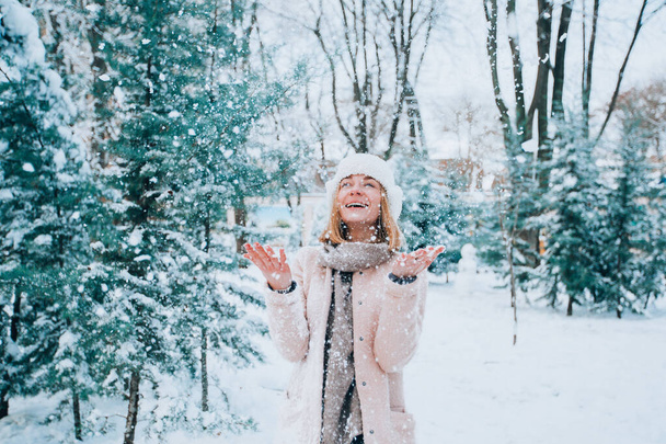 jong meisje lacht en gooit sneeuw in een winter besneeuwd park. sneeuwvlok op de voorgrond - Foto, afbeelding