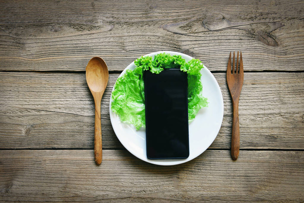 Essenslieferung online bestellen Smartphone auf dem Teller und auf dem rustikalen Holztisch mit Salatgemüse, Aufruf zur Lieferung mobiles Bestellkonzept - Foto, Bild