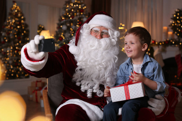 Santa Claus and little boy taking selfie in room decorated for Christmas - Фото, зображення