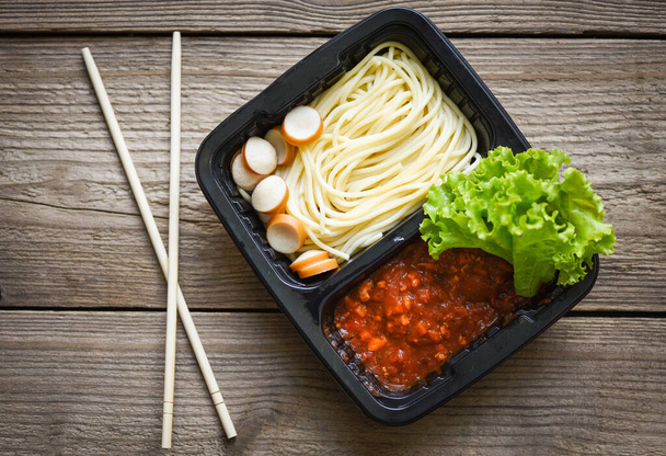 Szolgáltatás élelmiszer rendelés online szállítás Spagetti olasz tészta és paradicsom mártással kolbásszal a dobozon, élelmiszer szállítás elvitelre dobozok csomag fa asztalra otthon - tetejére nézet  - Fotó, kép