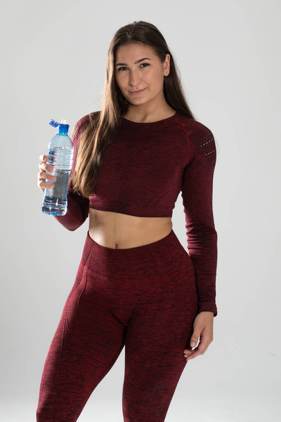 πορτρέτο του όμορφη νεαρή ταιριάζει γυναίκα πόσιμο νερό κατά τη διάρκεια traning στο γυμναστήριο, νεαρή όμορφη κοπέλα με μεταλλικό νερό (απομονώνονται σε λευκό) - Φωτογραφία, εικόνα