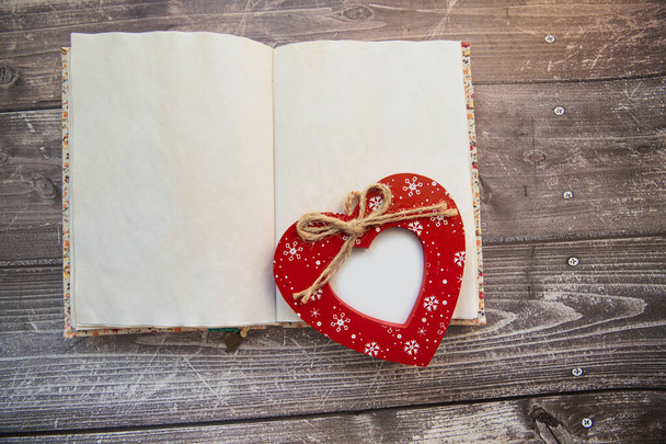 Красная рамка в форме сердца лежит на открытом блокноте, вид сверху. День святого Валентина - Фото, изображение