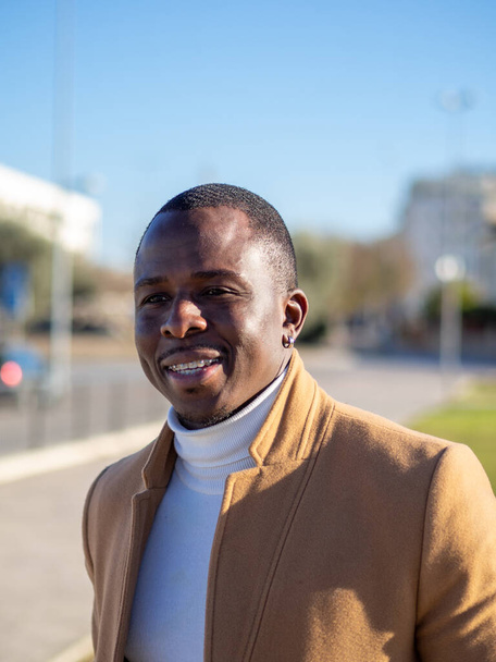 A shallow focus of an adult African male wearing a white turtleneck with a beige coat outdoors - Fotó, kép