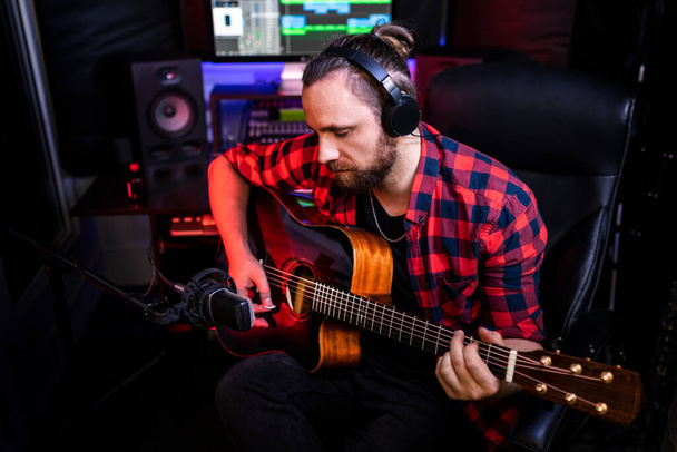 Hipster-Mann mit Bart und Kopfhörer spielt Gitarre und singt seinen neuen Song im Stereo-Studio, um brandneuen Track aufzunehmen - Foto, Bild