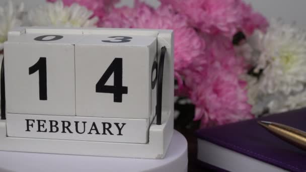Desktop calendar with the date of February 14 and a bouquet of beautiful flowers. Delicate chrysanthemums for Valentine's Day. Handmade wood cube with date month and day. planning for the day. - Footage, Video