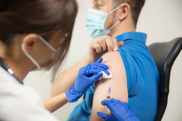 Κοντινό πλάνο γιατρός ή νοσηλευτής που χορηγεί το εμβόλιο στον ασθενή χρησιμοποιώντας τη σύριγγα που ενίεται στο νοσοκομείο - Φωτογραφία, εικόνα
