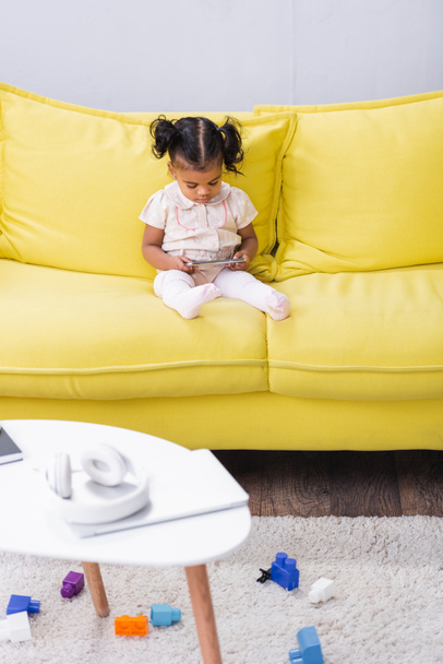 toddler african american girl using smartphone while sitting on sofa - Fotó, kép