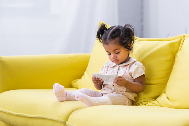 toddler african american girl using smartphone while sitting on couch - 写真・画像