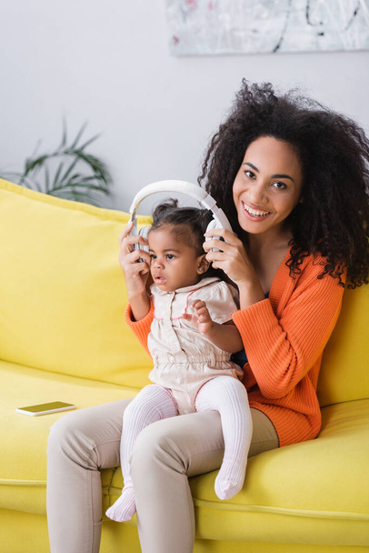 happy african american mother wearing wireless headphones on toddler daughter  - Foto, Imagen
