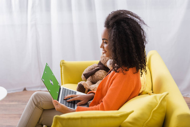 side view of happy african american freelancer using laptop with green screen at home - Fotó, kép
