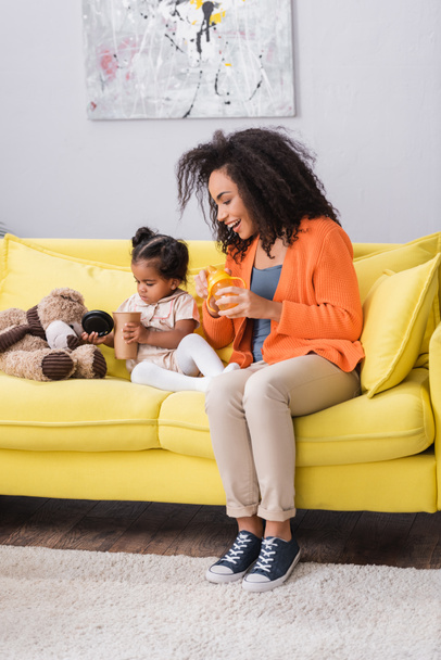 cheerful african american mother holding baby bottle near toddler daughter with empty paper cup  - Foto, Bild