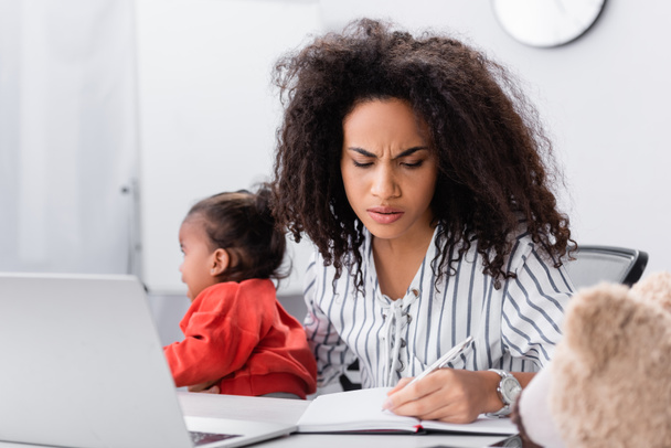 stressed african american mother holding in arms crying toddler daughter while working from home  - Photo, image