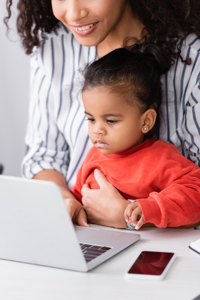 Afrykańska amerykańska matka siedzi z małą córeczką i używa laptopa na biurku - Zdjęcie, obraz