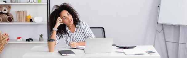pensive african american woman writing in notebook near gadgets on desk, banner - Fotografie, Obrázek
