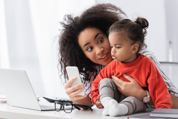 afro-amerikai anya mutatja okostelefon lánya az asztalon - Fotó, kép