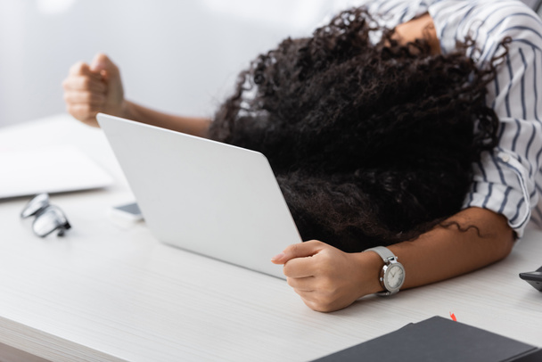 african american woman covering face while lying on laptop at home - Photo, Image