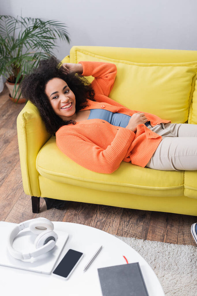 cheerful african american woman chilling on yellow couch - Foto, Bild