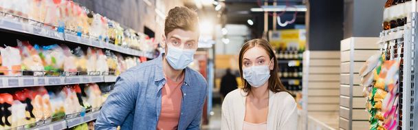 junges Paar in Arztmasken blickt im Supermarkt in die Kamera, Transparent  - Foto, Bild