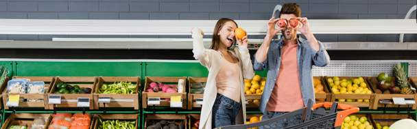 Young couple holding fruits near shopping cart in supermarket, banner  - Φωτογραφία, εικόνα