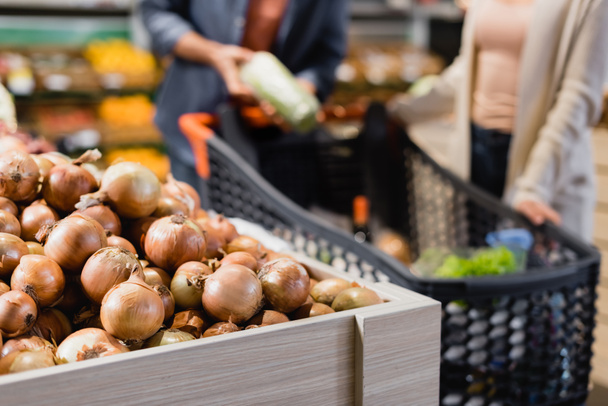 Vista recortada de cebollas cerca de pareja sobre fondo borroso en el supermercado  - Foto, Imagen