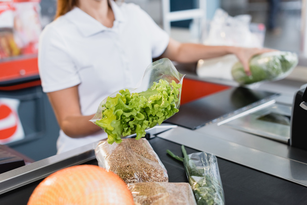 Cropped view of lettuce in hand of cashier in supermarket on blurred background  - Zdjęcie, obraz