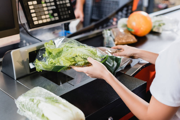 Обрезанный вид молодого кассира, держащего свежий салат на кассе супермаркета - Фото, изображение