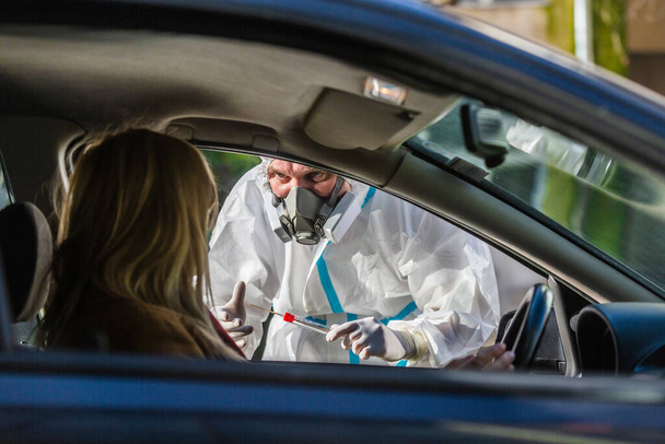 Nő ül az autóban, várja, hogy az egészségügyi dolgozó hajtson végre autós COVID-19 tesztet, vesz orrmintát az autó ablakán keresztül, PCR diagnosztika Coronavirus, orvos PPE holding teszt készlet. - Fotó, kép