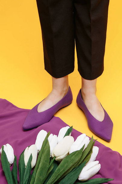 Beautiful female legs are dressed in stylish violet flat shoes. violet sandals on a yellow background. - Фото, изображение