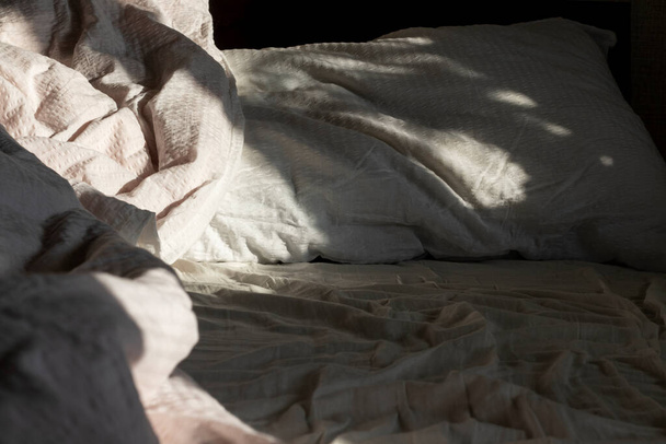 Morning shadows illuminate the empty bed with white crumpled linen. Close-up. - Φωτογραφία, εικόνα