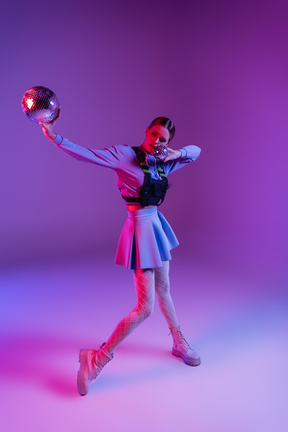full length of woman in skirt holding disco balls on purple - Zdjęcie, obraz