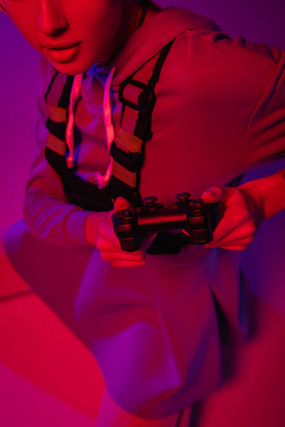 KYIV, UKRAINE - NOVEMBER 27, 2020: cropped view of young woman holding joystick on purple  - 写真・画像