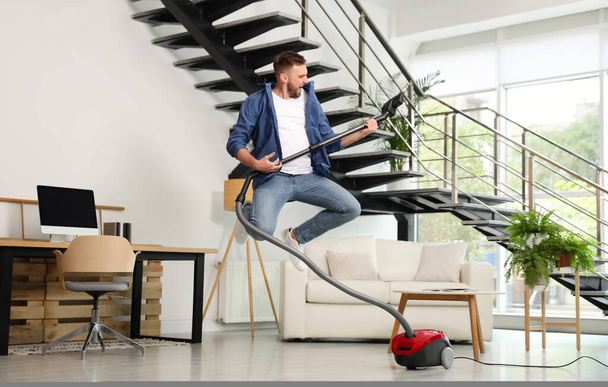 Young man having fun while vacuuming in living room - Foto, Imagen